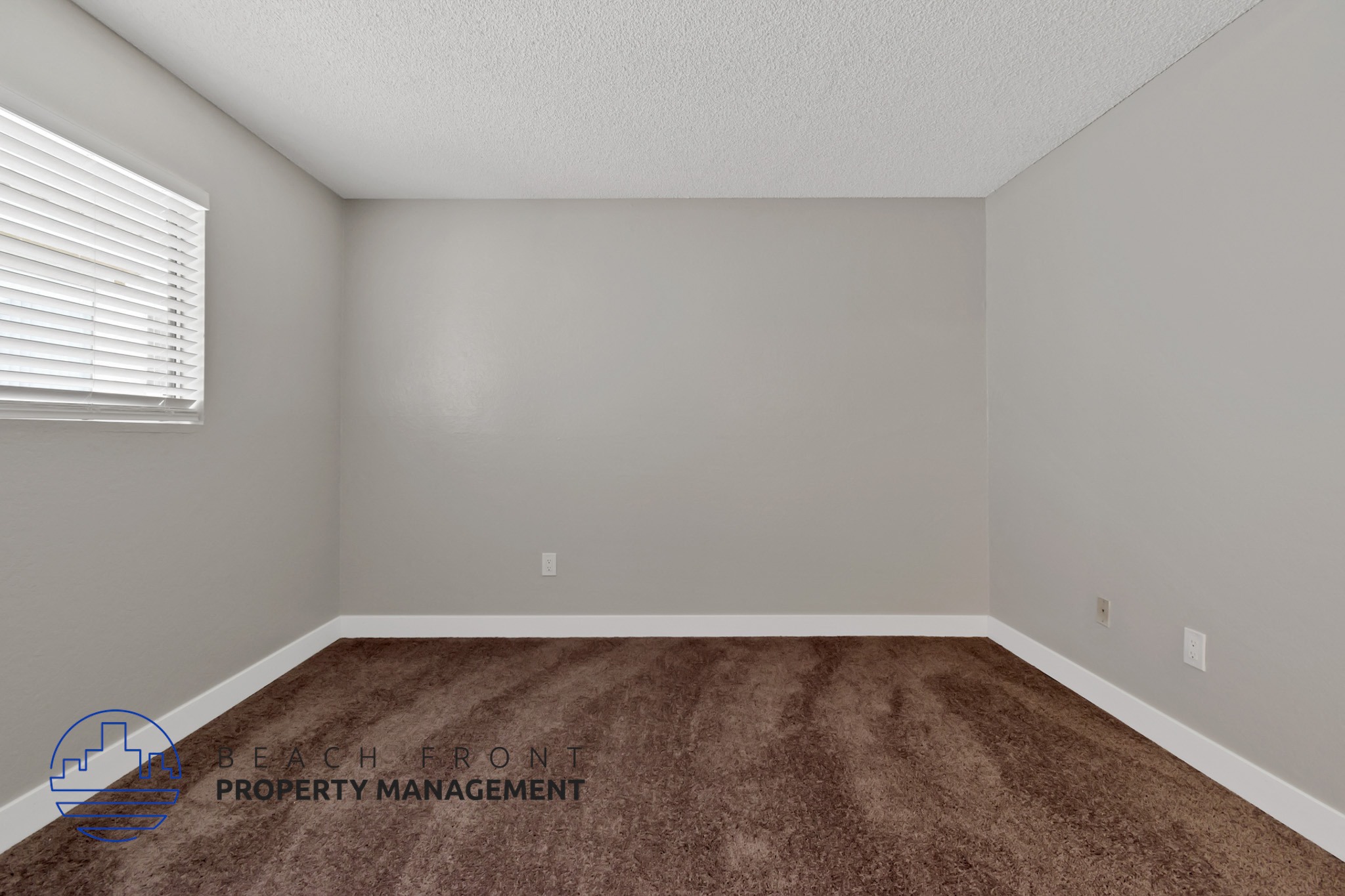 A room with a brown carpet and a window with blinds.